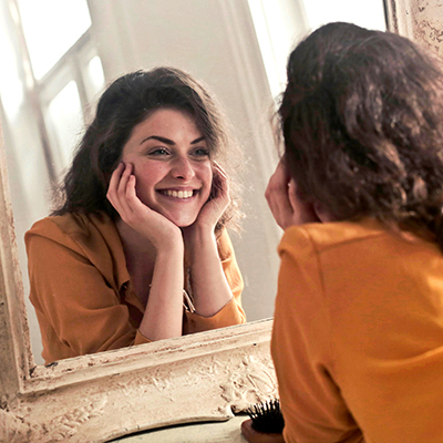 Beeld van een jonge vrouw die glimlachend in de spiegel kijkt